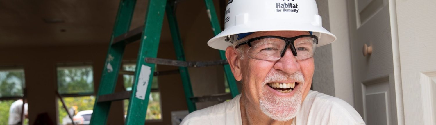 man in a hardhat smiling with a hardhat in front of a ladder