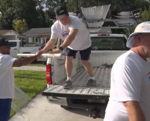 man on the back of a truck getting tools handed to him from another man