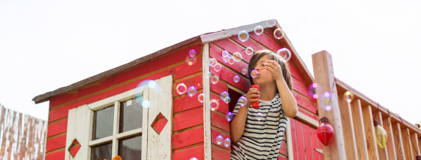 kid blowing bubbles outside of a playhouse window