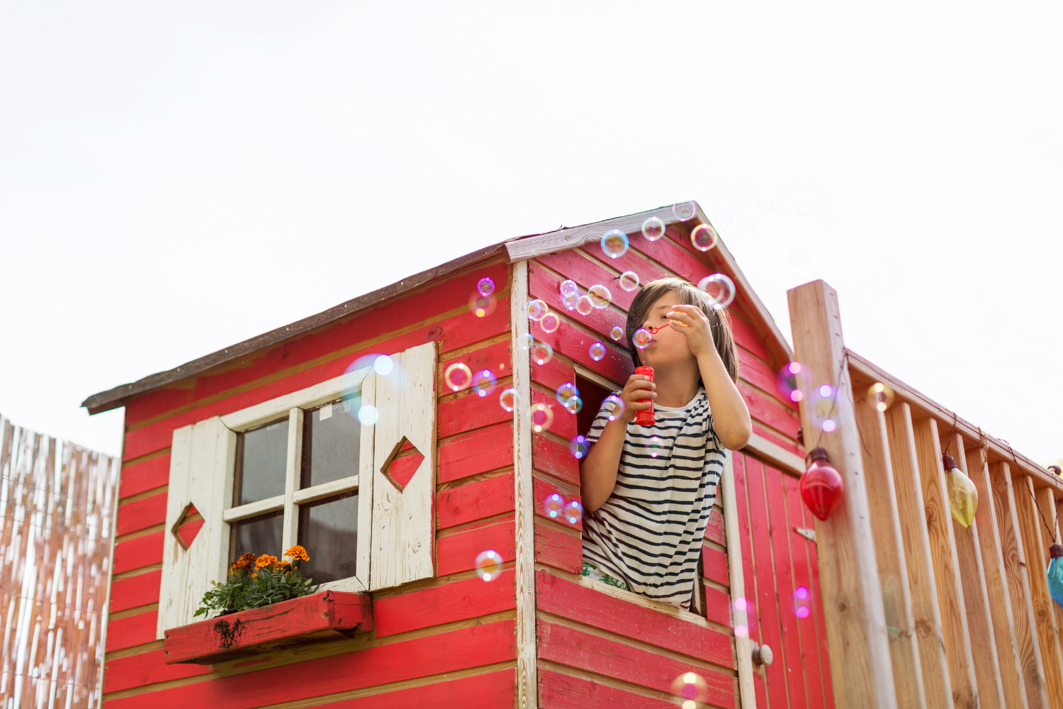 kid blowing bubbles outside of a playhouse window